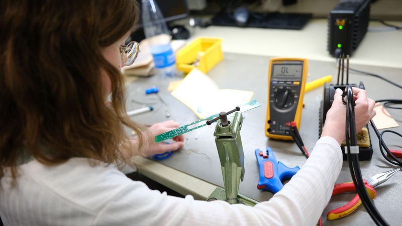 Ein Mädchen sitzt an einem Werkstatttisch und benutzt ein Messgerät.